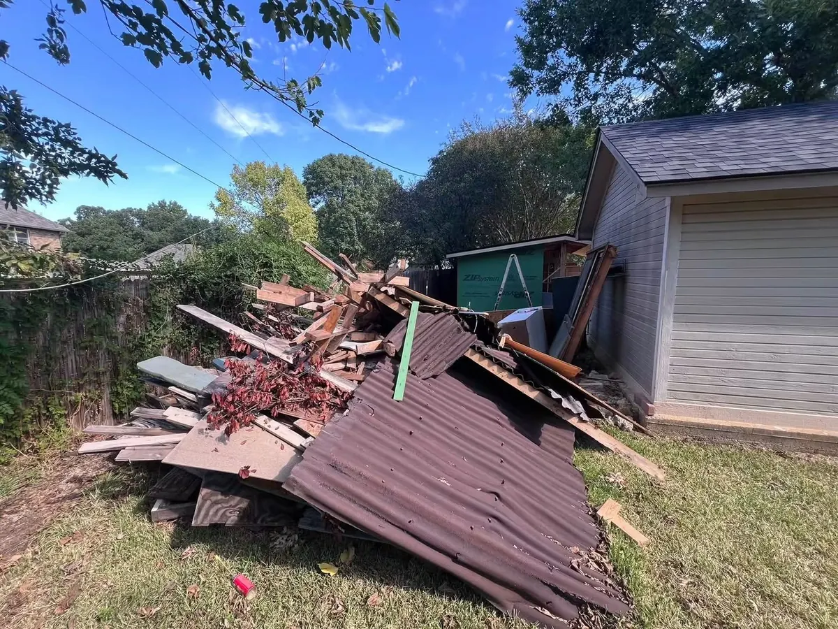 A torn-down shed roof and lumber piled in a backyard
